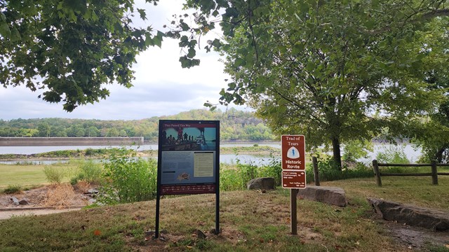 An interpretive exhibit standing in front of a long, flat river.