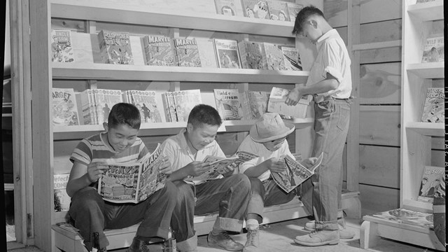 Three boys browse wooden shelves with comic books