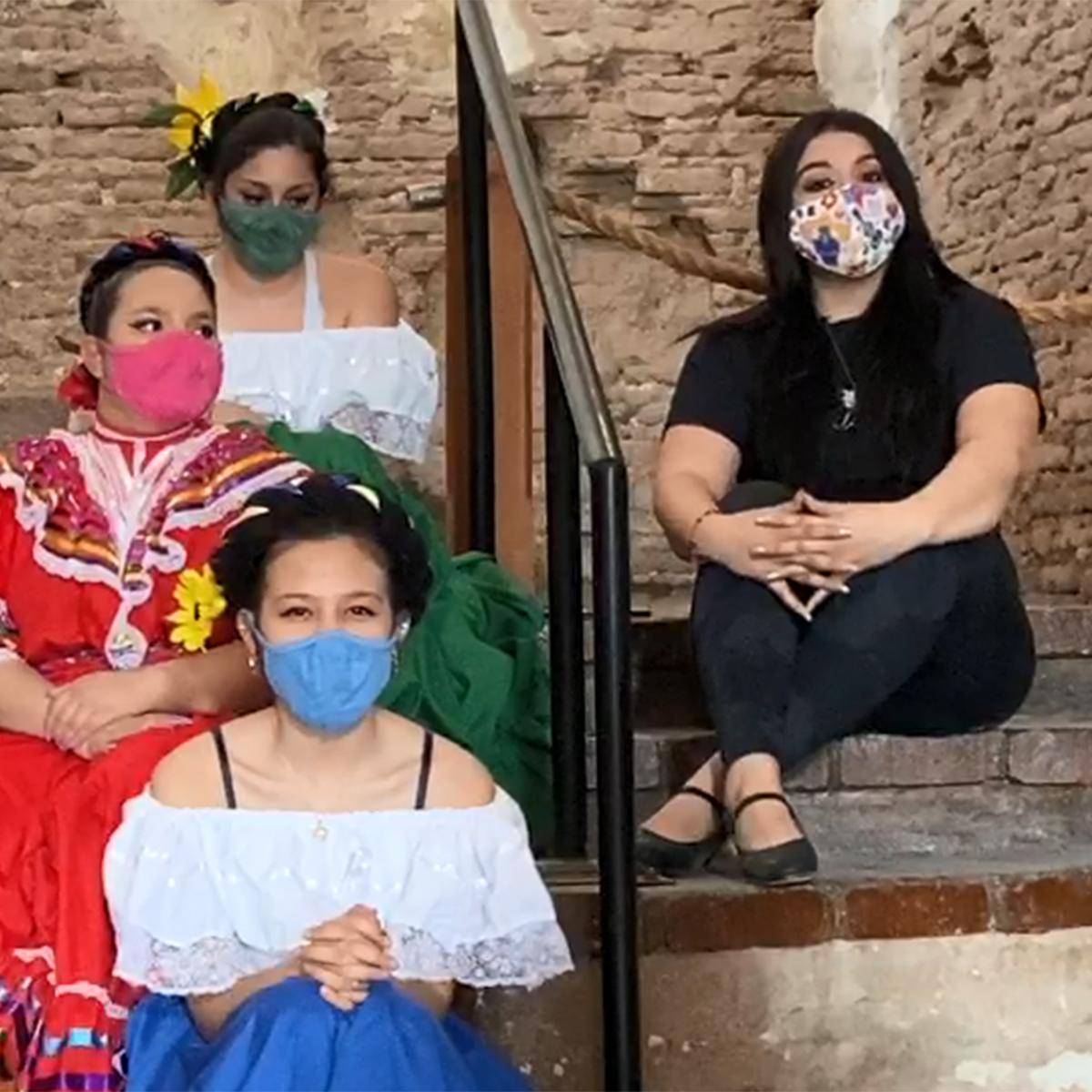 dance teacher with students in colorful folklórico costumes seated on steps inside the church