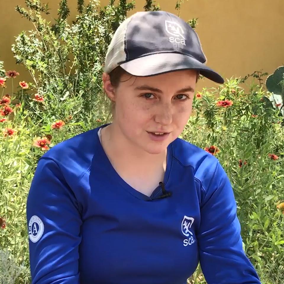 volunteer in SCA uniform sitting in front of desert garden plants
