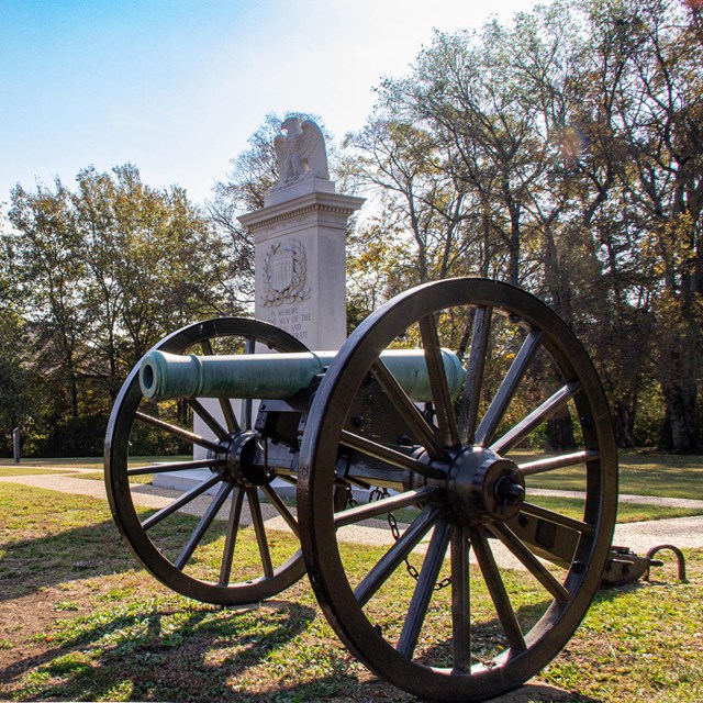 A metal canon in front of a stone monument.