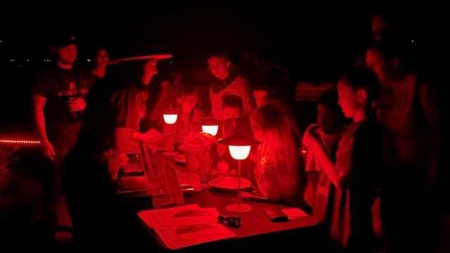 Red lights illuminate a ranger talking to children at a table.