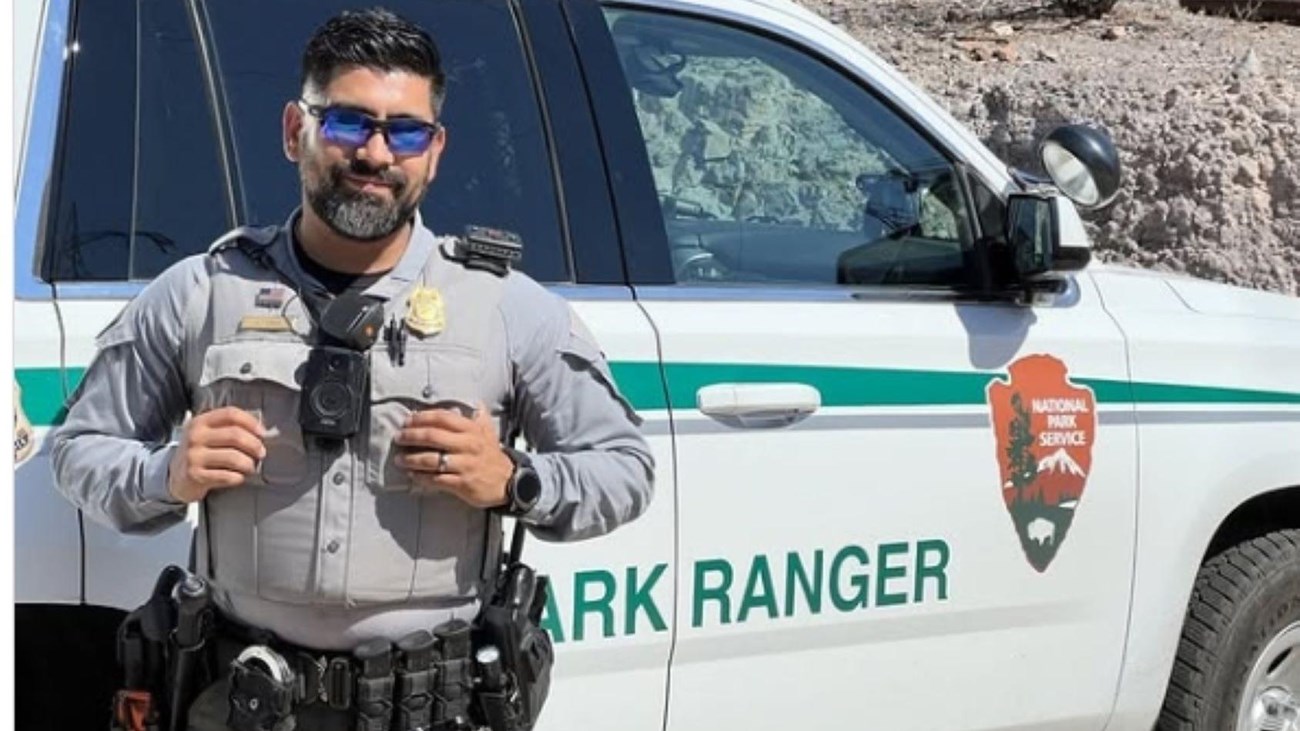 A NPS Law Enforcement Park Ranger poses next to a park ranger truck smiling with sunglasses.