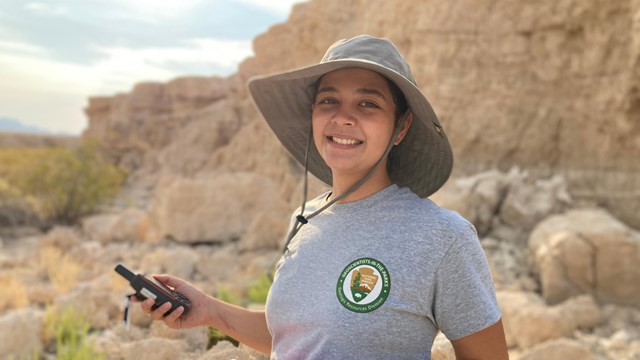 A young woman stands against desert badlands with a clipboard and GPS unit