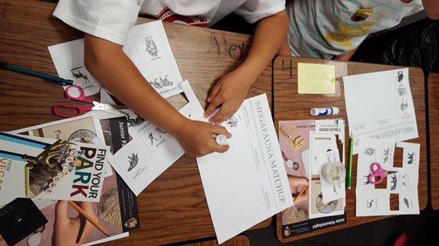 Kids hands on a table working with junior paleontologist books