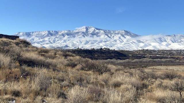 winter landscape at Tuzigoot, with snowy mountains, a blue sky, and yellow grass