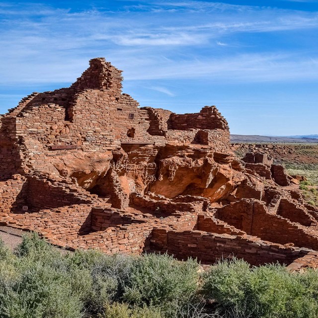 remains of a red stone pueblo under a blue sky