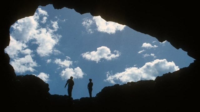 Looking out at the sky and two visitors from within the darkness of a cave