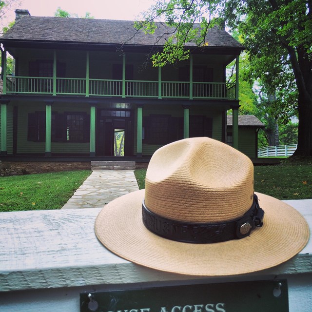 Ranger Hat on a white fence with a green house in the background.