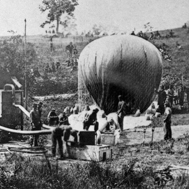 Several Union soldier fill a balloon using two large hydrogen generators. 