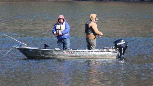 Two men in motorboat with fishing rods in the middle of the river.