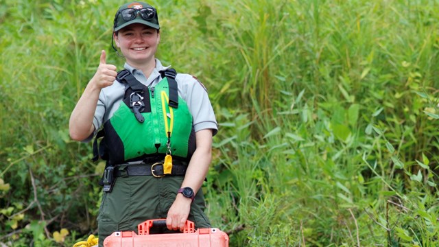 Park Ranger in life jacket smiles at camera while holding first aid kit.