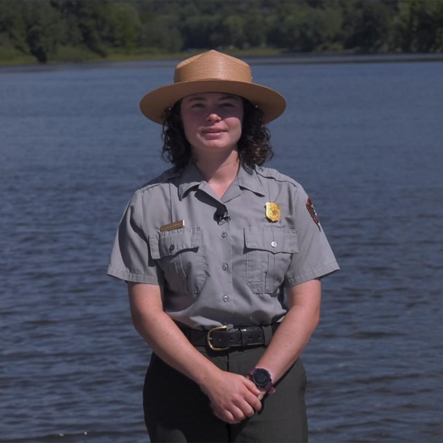 Park ranger standing in front of blue river.