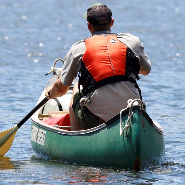 park ranger in life vest paddling in canoe on the water with back to the camera
