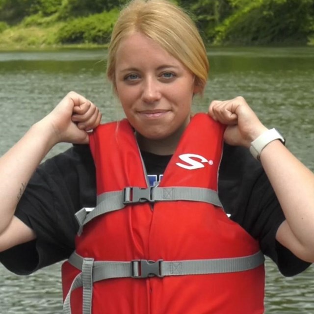 Woman wearing life jacket buckled snugly closed. She tugs on shoulders but it doesn't give.