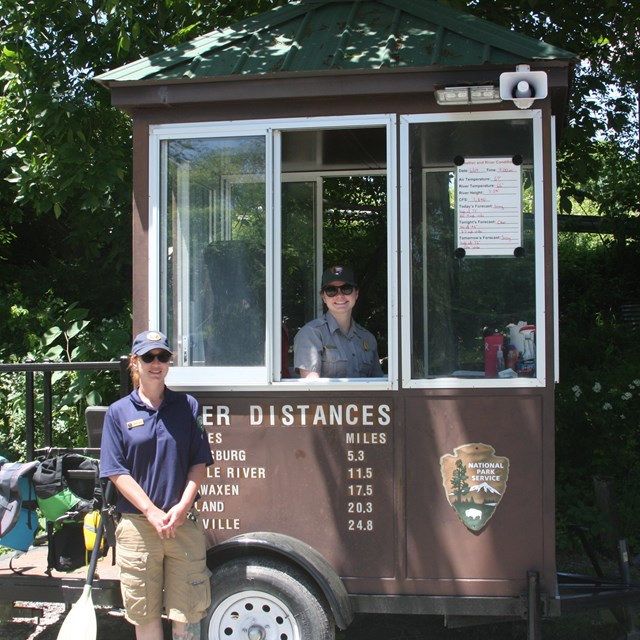 Brown national park information kiosk on wheels. One staff stands in kiosk looking out window.