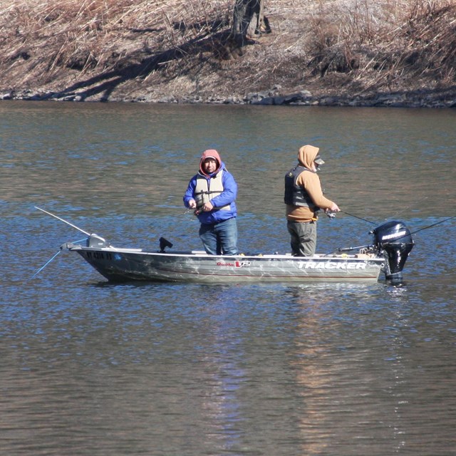 Two men in motorboat with fishing rods in the middle of the river.