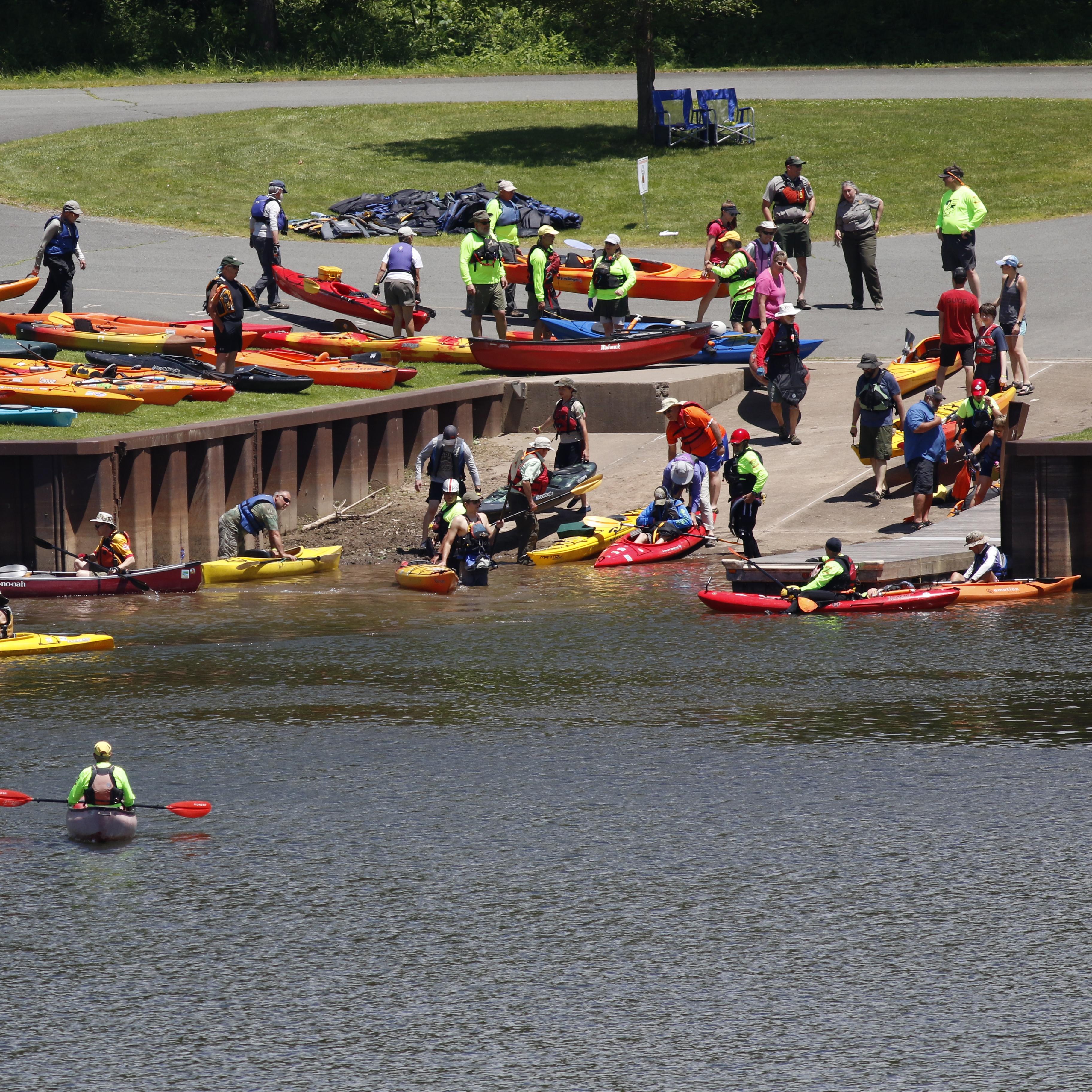 Public access area into a river. Paved ramp inclines into the river. People with kayaks enter water.