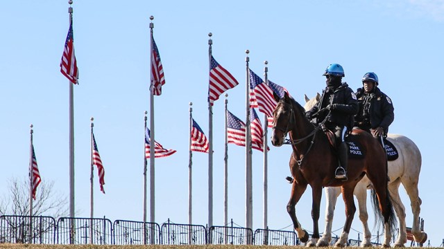 Two mounted U.S. Park Police officers on horses near a circle of U.S. flags