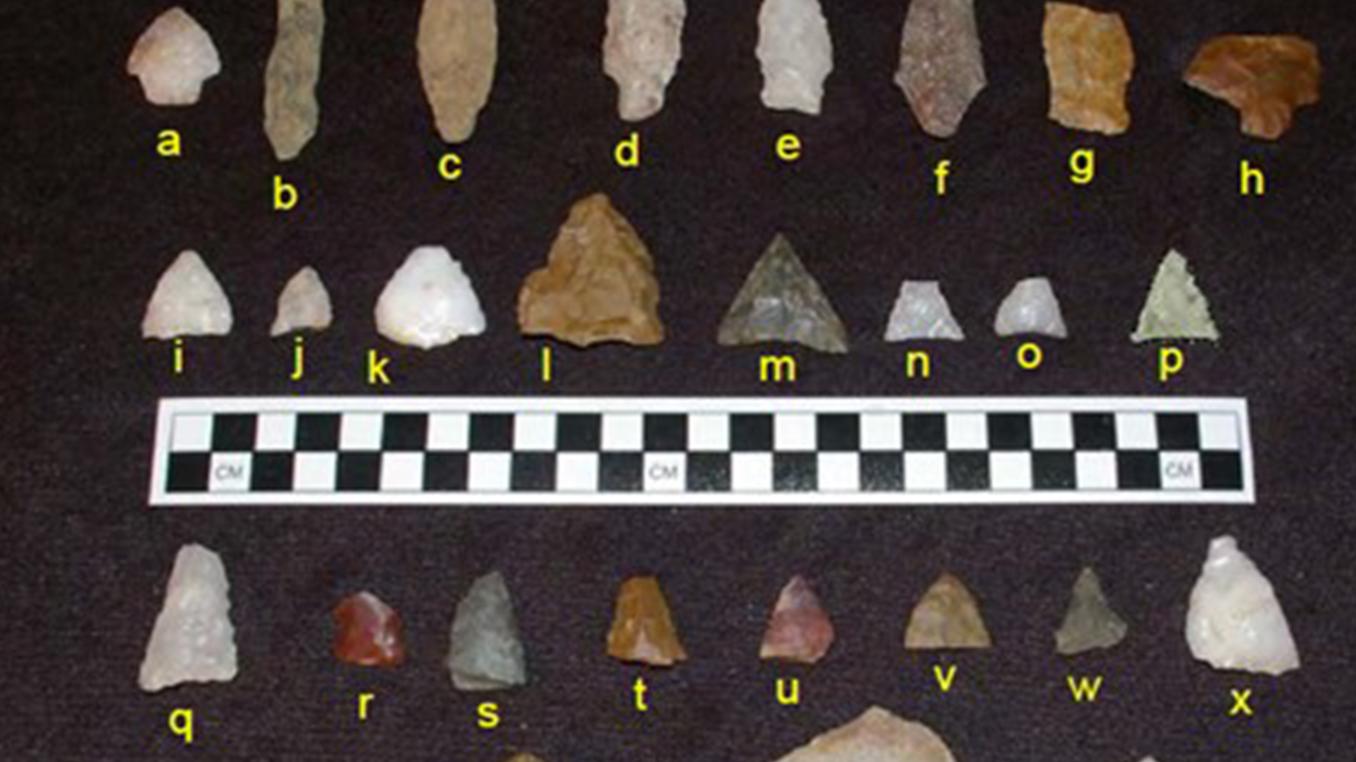 photograph of assorted stone artifacts on black background marked with letters and a ruler