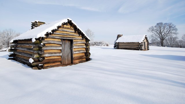 Two log huts with snow cover on  ground and hut roofs