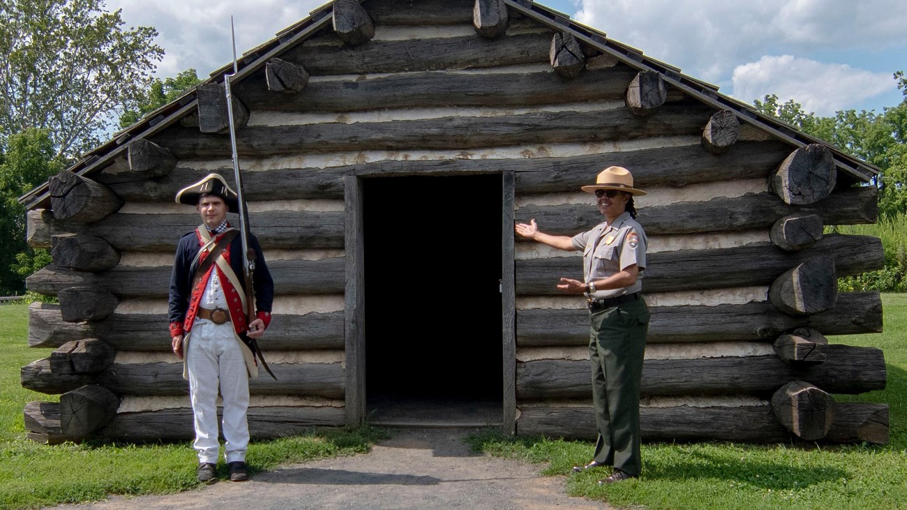 two rangers, one in a soldier uniform and another in the NPS uniform stand outside a hut