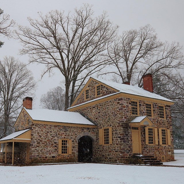 A stone house in the snow surrounded by tall trees. Washington's Headquarters.