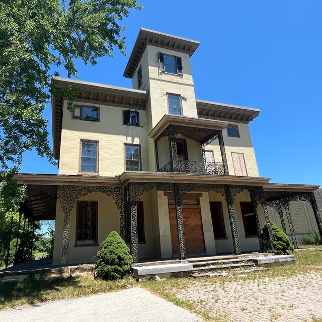 A large three story mansion with a cupola and an ornate ironwork porch.