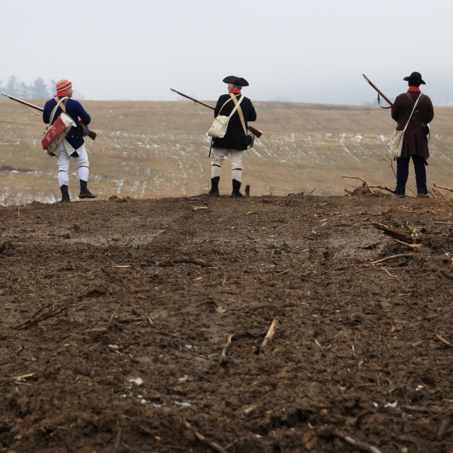 Reenactors stand looking over mowed meadows in the winter.