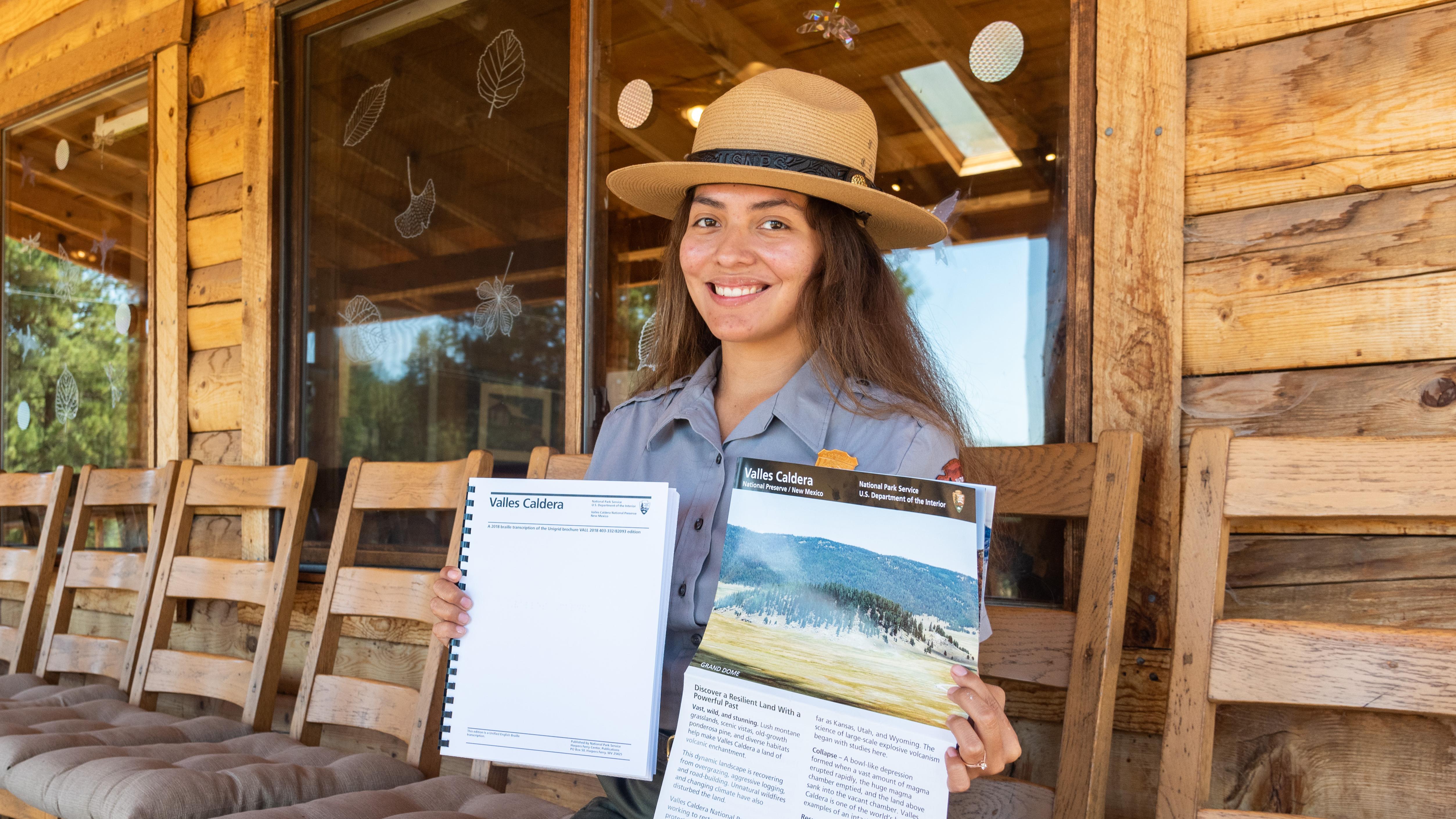 A park ranger holds up a large print brochure and a Braille brochure.
