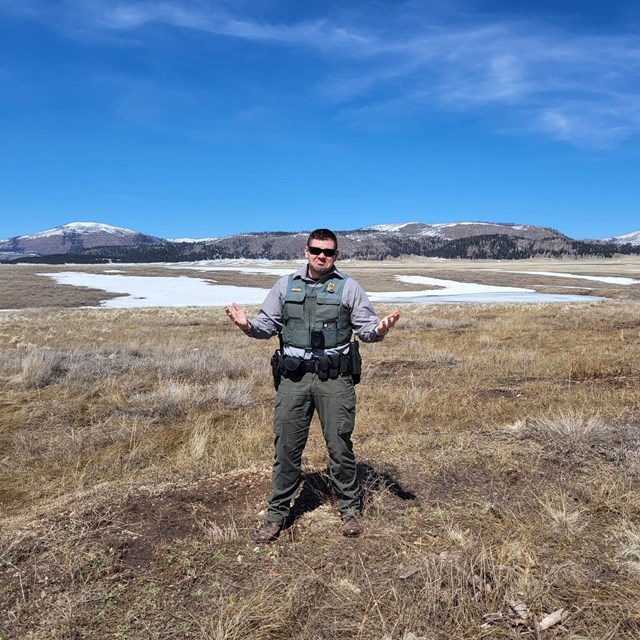 A park ranger stands in a valley with patchy snow.