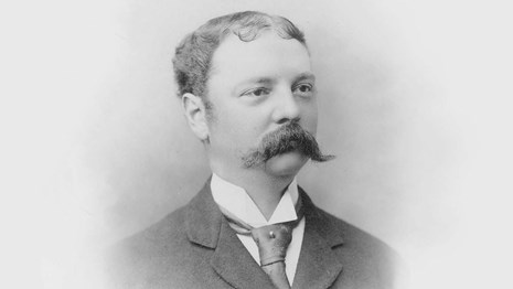 A head and shoulders photographic portrait of a man with handlebar mustache.
