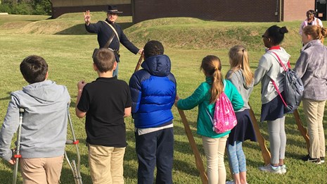 A park ranger dressed as a Union soldier teaching school children how to hold wooden muskets.