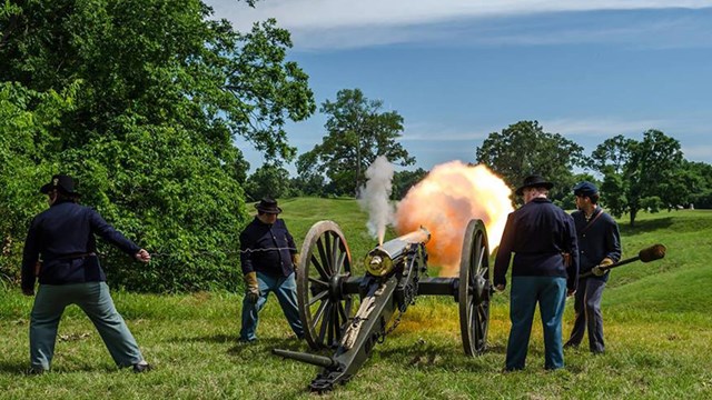 A group of people in Civil War uniforms shooting a cannon.