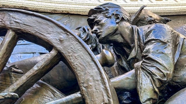 A bronze relief sculpture of man behind a cannon