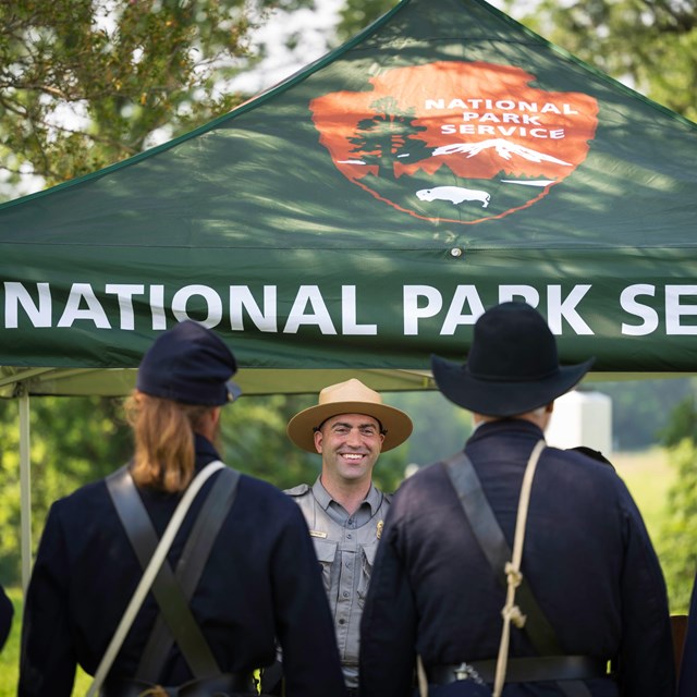 A ranger faces towards living history staff members dressed in period clothing