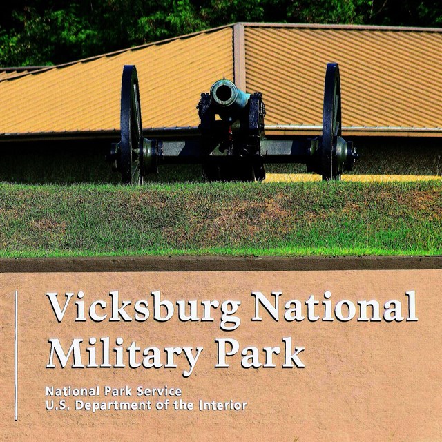 A cannon sits on top of a hill with the park entrance sign below.