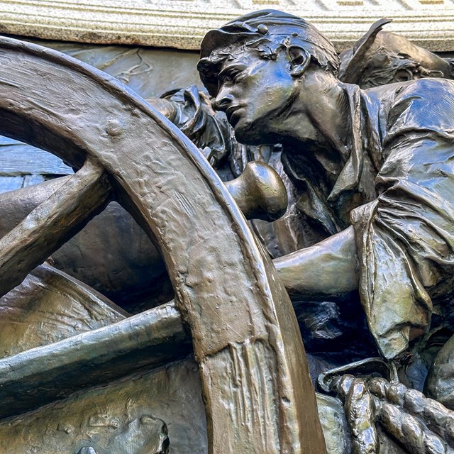 A bronze relief sculpture of man behind a cannon