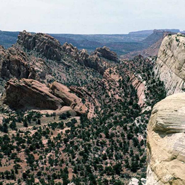 Photo of tilted rock beds forming mountains and cliffs in an arid landscape.