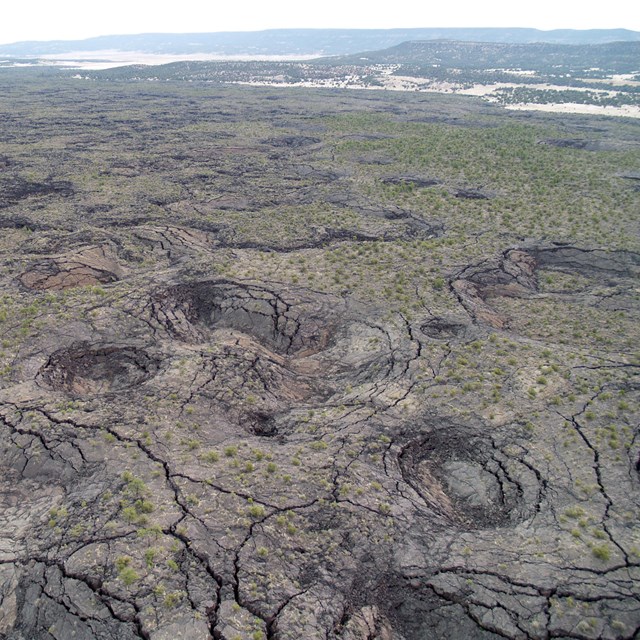 Aerial photo of a volcanic landscape of lava covered ground with plateaus, cracks, and pits