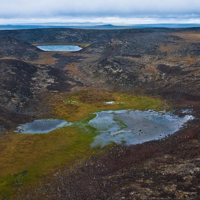 two water-filled craters surrounded by black rock and tundra