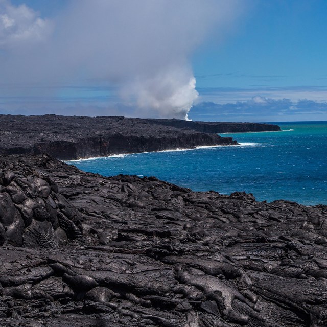 lava field along an ocean shoreline with a distant plume of steam