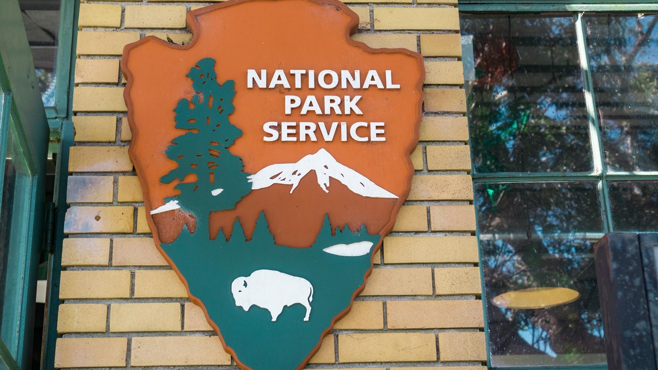 Photograph of NPS arrowhead logo on the exterior of a brick building.