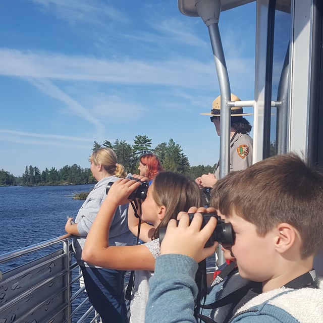 Image of four children using binoculars looking at the lake
