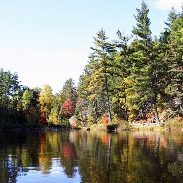 Brightly-colored trees are reflected on the water along the shore of a scenic lake.