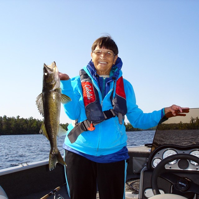 A woman stands in a motorboat holding a large walleye that she recently caught.