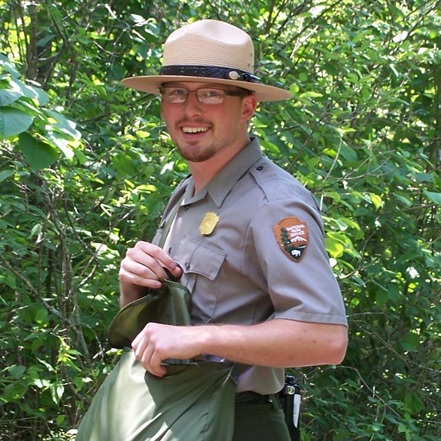 A ranger stands on a trail in the woods.