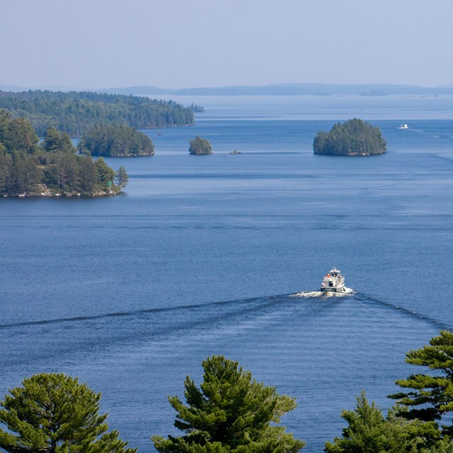 A large boat makes its way across a scenic, blue lake with islands along the horizon.