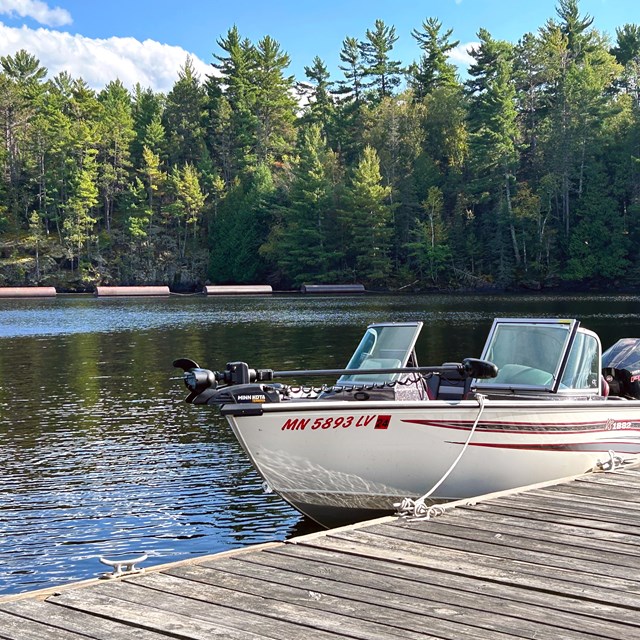 A white boat with red stripes shines in the sun, docked in a picturesque bay.