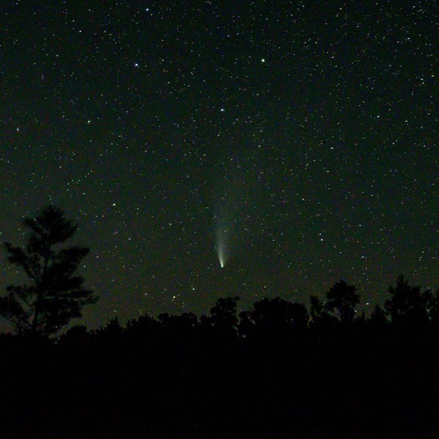 A comet streaks against the black sky, leaving a long plumed 